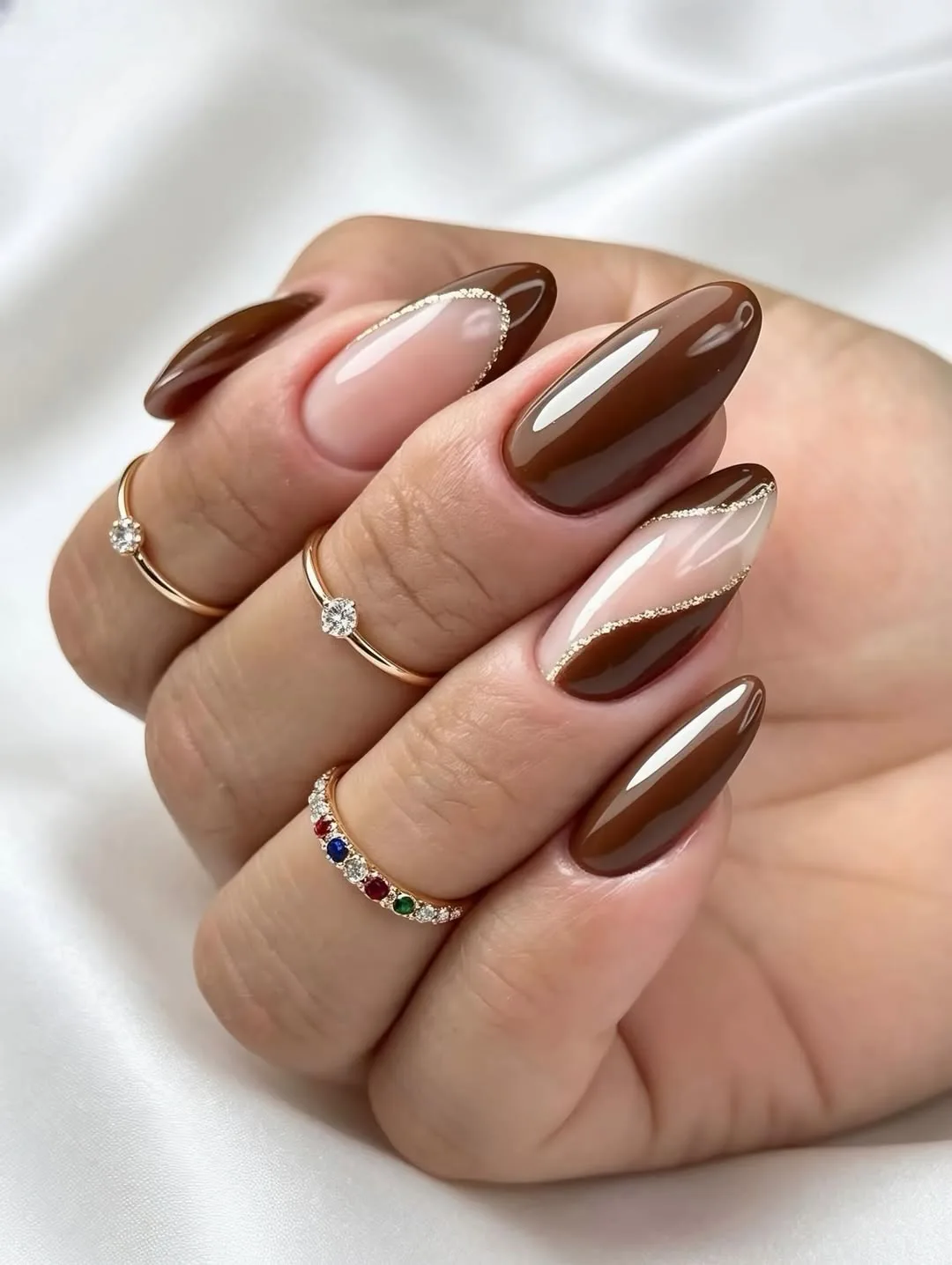Glossy mocha-brown almond nails with cream swirl-French detailing and gold-glitter liner on white silk